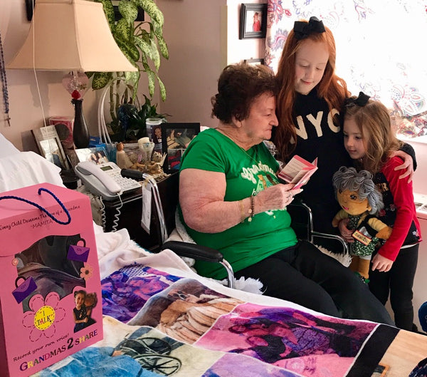 Woman in green shirt reading a book to two children in a home setting with a pink gift bag and colorful blanket.
